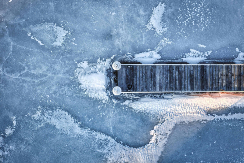 Frozen lake with thick ice sheets lifting and damaging wooden floating docks in winter