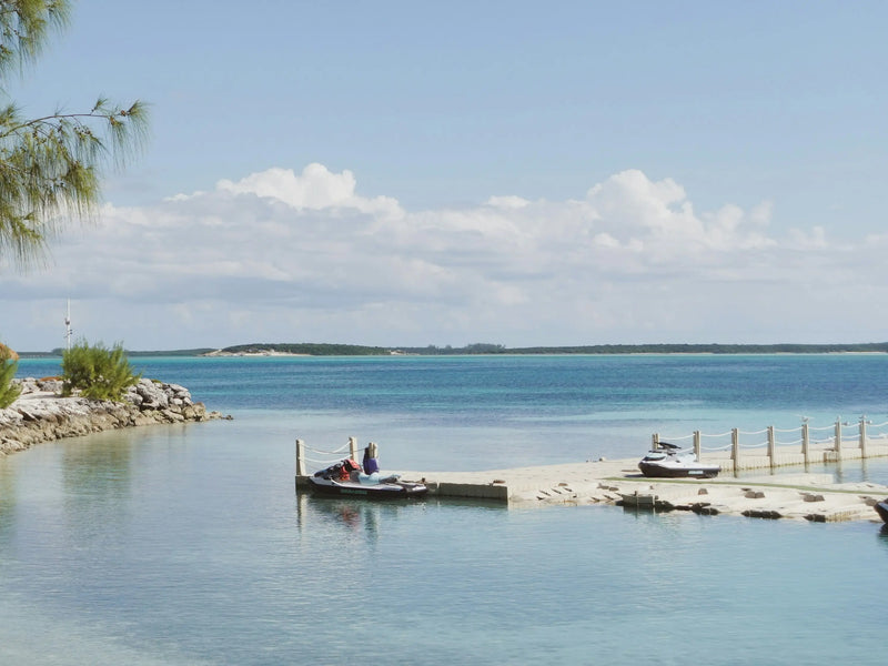 Jet skis parked on modular floating dock in crystal clear tropical waters with beach and island view