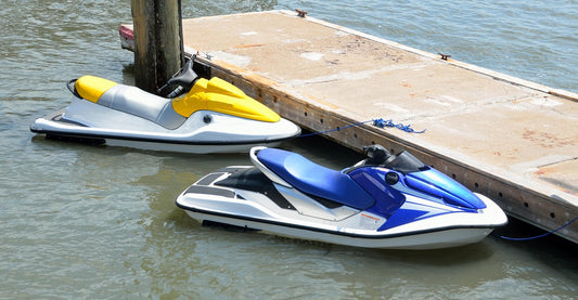 Two jet skis (yellow and blue) tied with ropes to a traditional fixed wooden pier, contrasting with the convenience of modern floating docks for jet ski